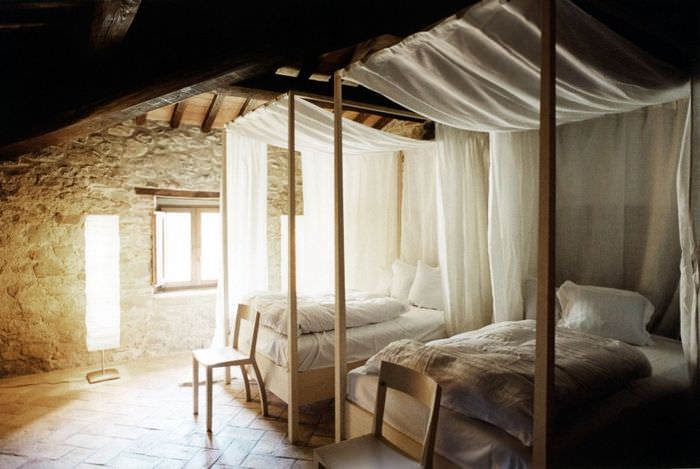 Кровати с простыми балдахинами в комнате с каменными стенами